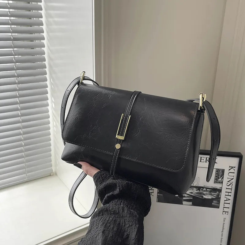 Rectangular flap shoulder bag with slim metal front detail — black held near window | BTendance
