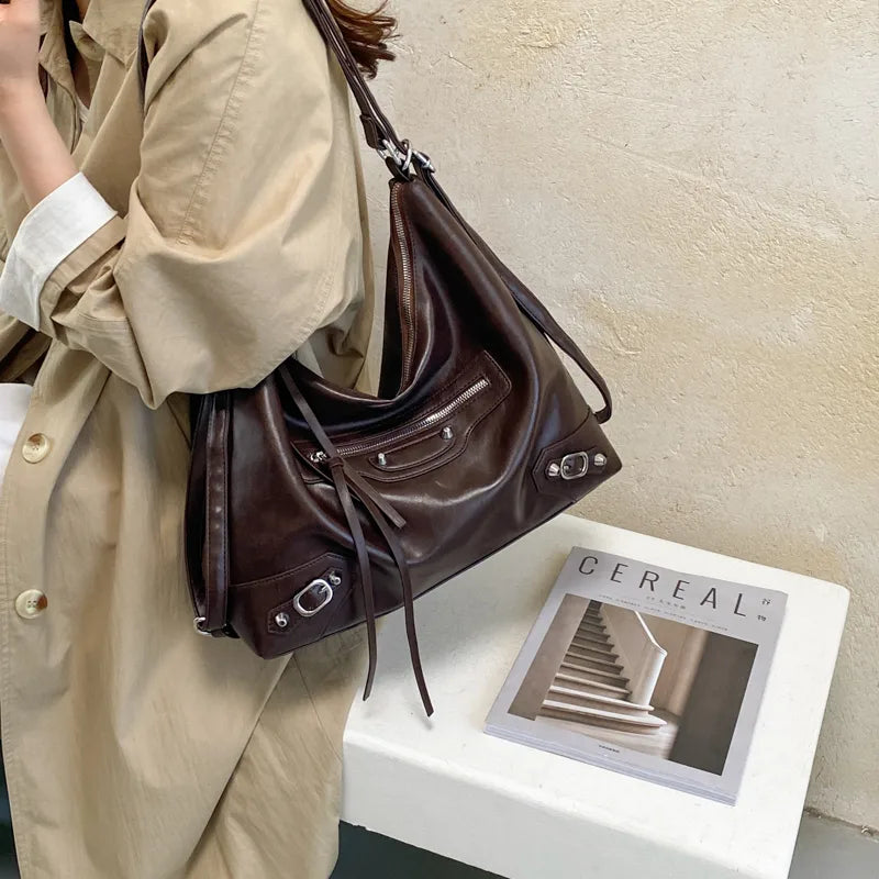 Slouchy shoulder bag with front zip and buckle details — dark brown worn over beige coat | BTendance
