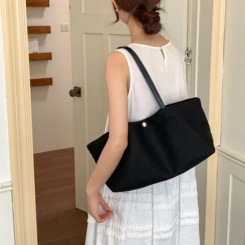 Wide canvas tote with contrasting dark shoulder handles — black worn with white dress | BTendance
