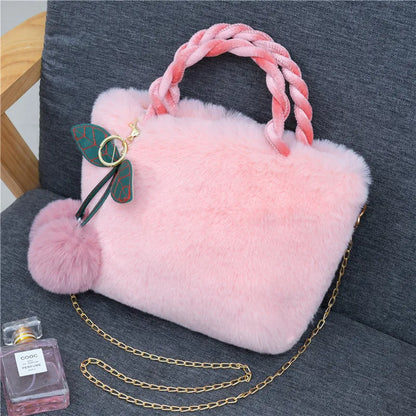 Plush handbag with twisted pink handles and pom-pom cherry charm — light pink on grey chair | BTendance