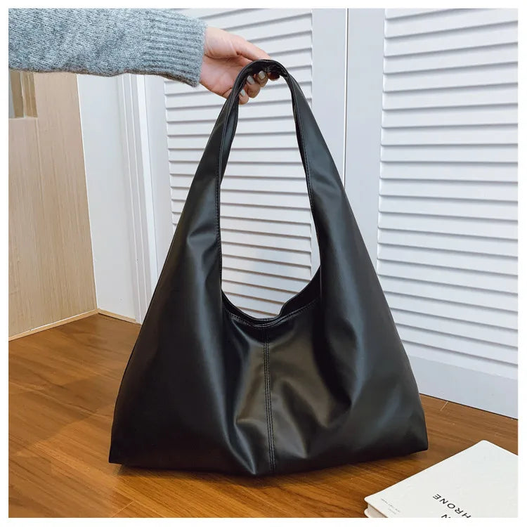 Slouchy shoulder tote with wide integrated strap — black held above wooden table | BTendance