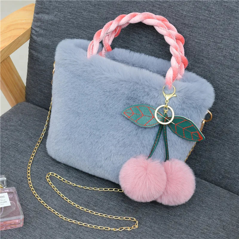 Plush handbag with twisted pink handles and pom-pom cherry charm — blue on grey chair | BTendance