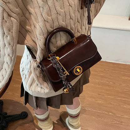 Structured top-handle flap handbag with round gold-tone clasp — brown worn crossbody with scarf accent | BTendance