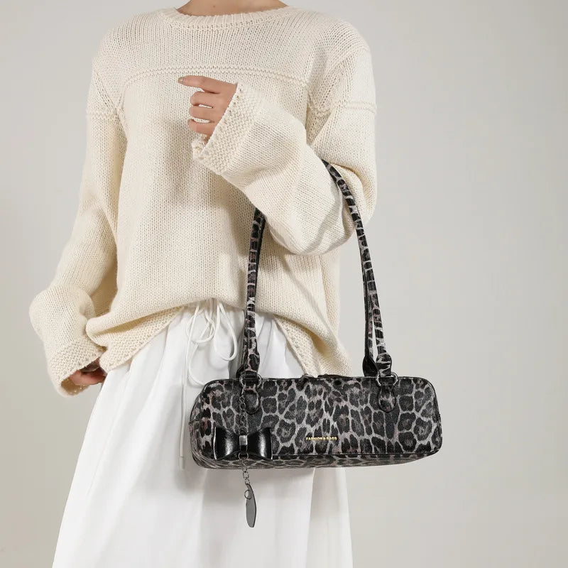 Leopard print shoulder bag with heart charm – Grey leopard bag held beside a cream outfit | BTendance