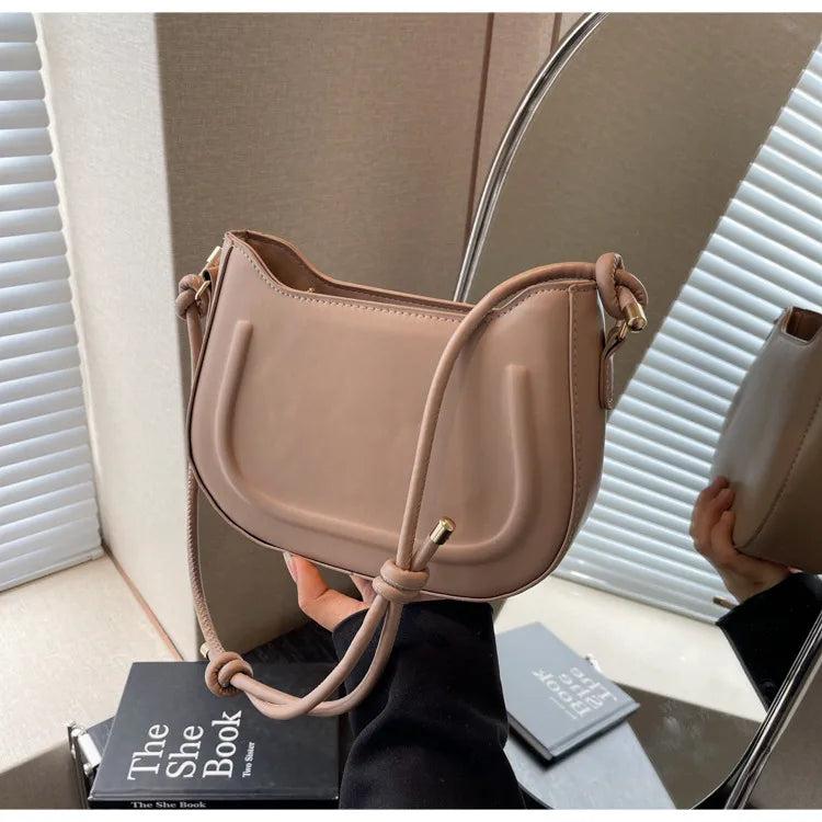 Curved shoulder bag with outlined front panel and knotted strap — tan held in front of mirror | BTendance