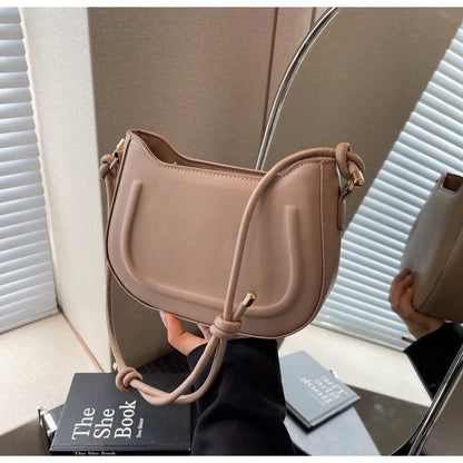 Curved shoulder bag with outlined front panel and knotted strap — tan held in front of mirror | BTendance