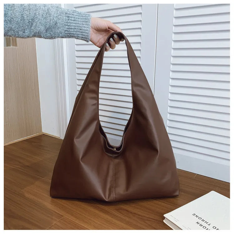 Slouchy shoulder tote with wide integrated strap — dark brown held above wooden table | BTendance