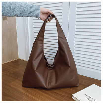 Slouchy shoulder tote with wide integrated strap — dark brown held above wooden table | BTendance