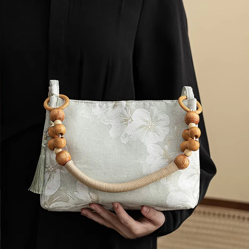 Floral shoulder bag with beaded handle – Pale green bag held against a black outfit | BTendance