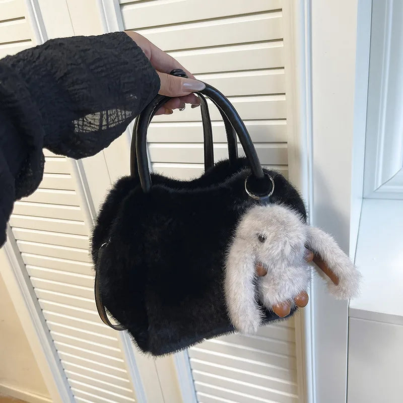 Plush top-handle handbag with rabbit charm — black held in one hand | BTendance