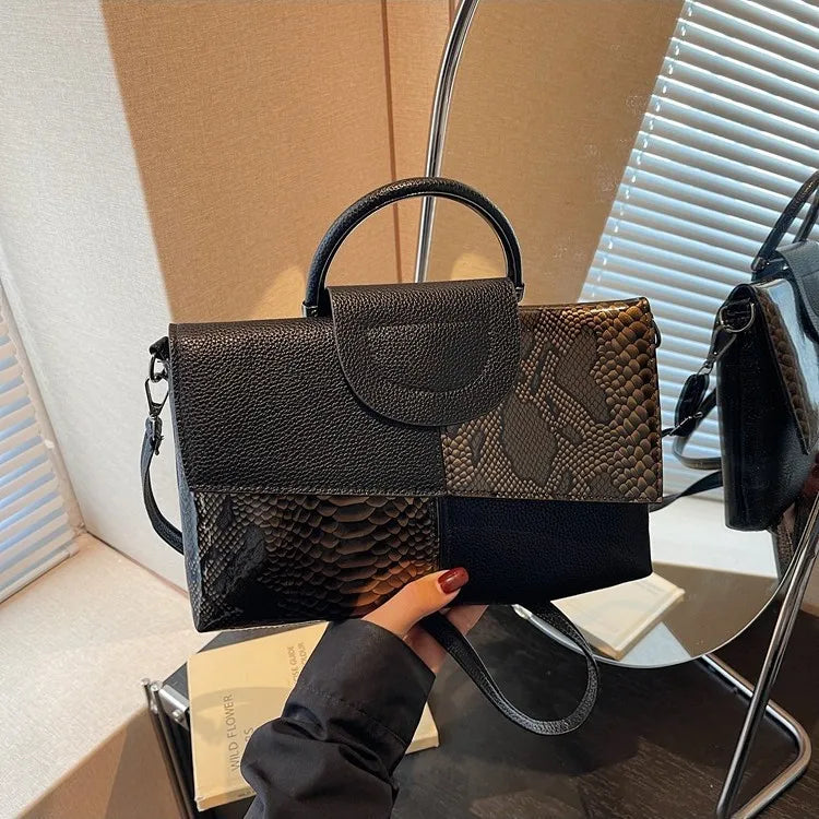 Structured handbag with contrasting reptile-texture panels — black and brown held in one hand | BTendance