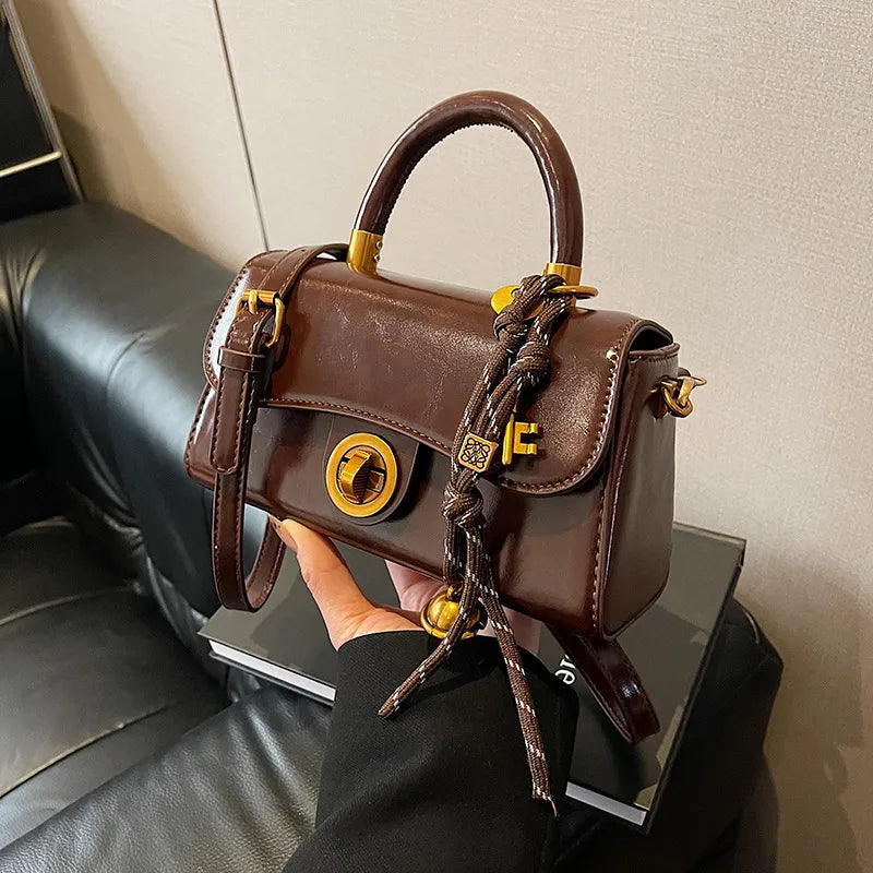 Structured top-handle flap handbag with round gold-tone clasp — brown with scarf accent held in one hand | BTendance