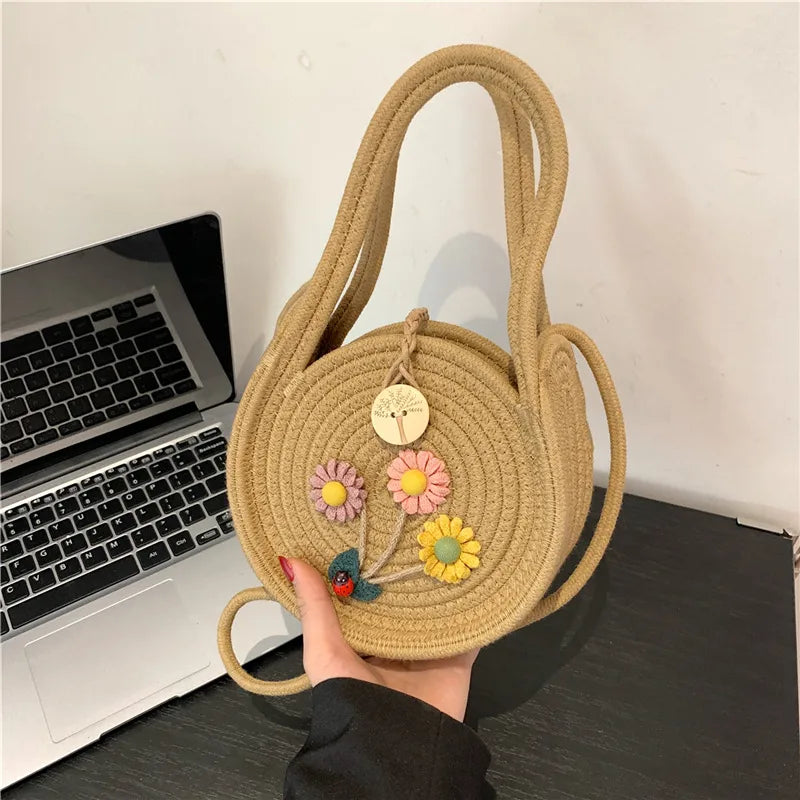 Round woven handbag with flower decoration – Tan flower bag held above a desk | BTendance