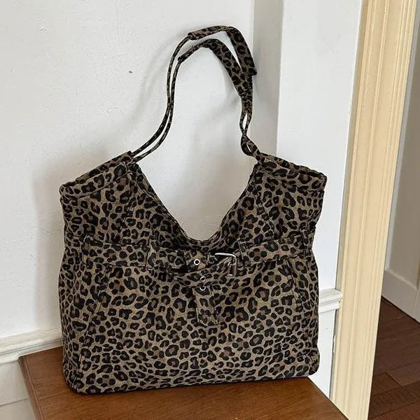 Leopard-print shoulder tote with front buckle detail — hanging beside wooden door | BTendance