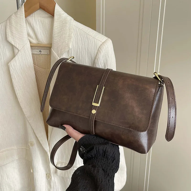 Rectangular flap shoulder bag with slim metal front detail — brown held beside white jacket | BTendance