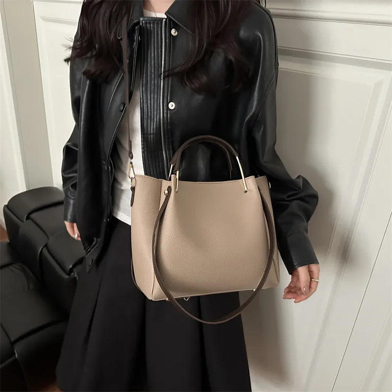 Textured bucket handbag with contrasting dark handles — taupe worn over black jacket | BTendance
