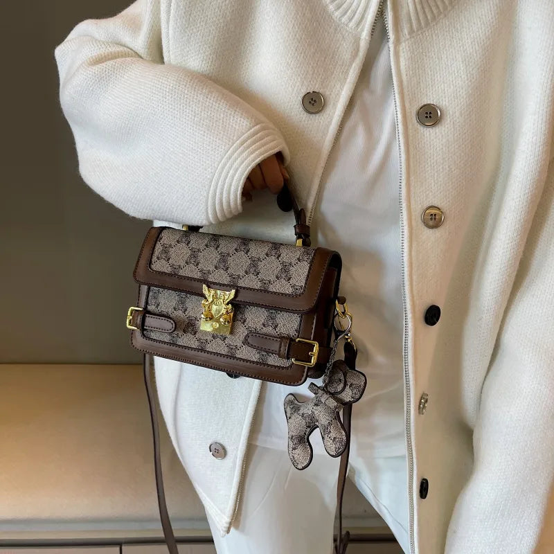 Bear pattern top handle bag with charm – Brown bag held against a cream outfit | BTendance