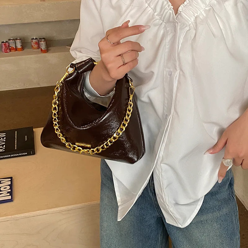 Soft handbag with gold tone chain – Brown bag held against a white blouse | BTendance