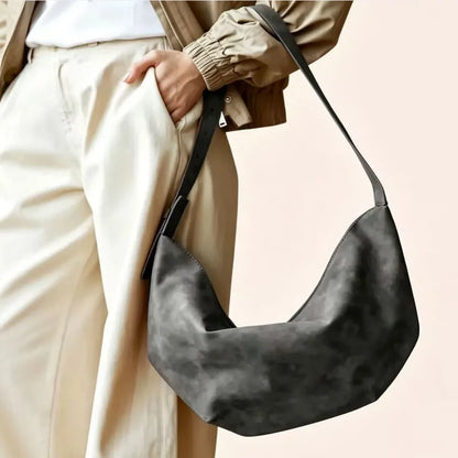 Crescent-shaped shoulder bag with adjustable strap — charcoal carried beside cream trousers | BTendance