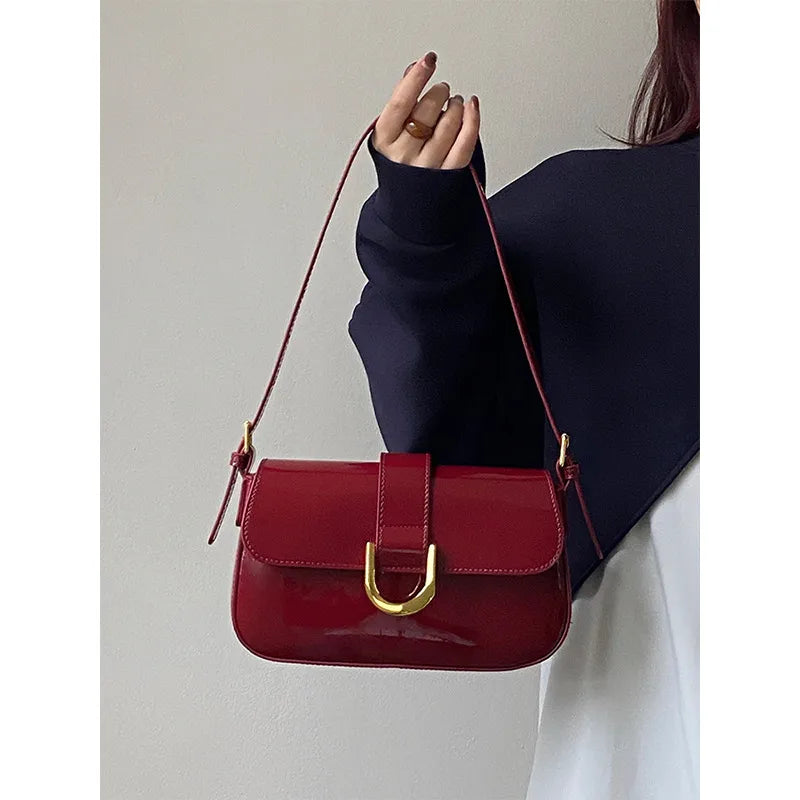 Flap shoulder bag with gold tone U clasp – Red bag held beside a dark sweater | BTendance