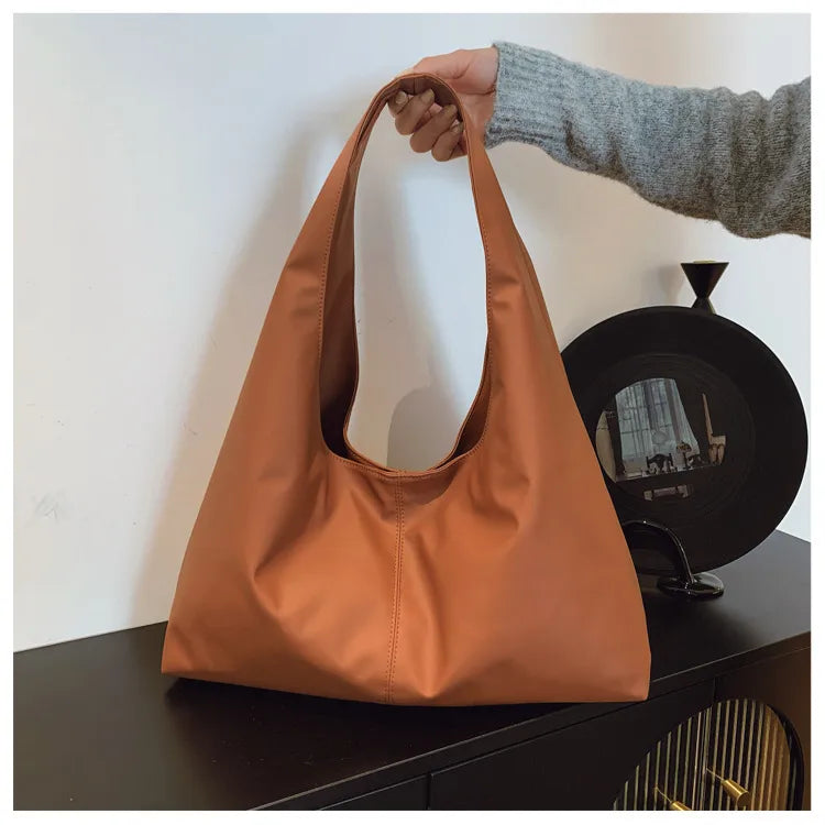 Slouchy shoulder tote with wide integrated strap — tan held above cabinet | BTendance