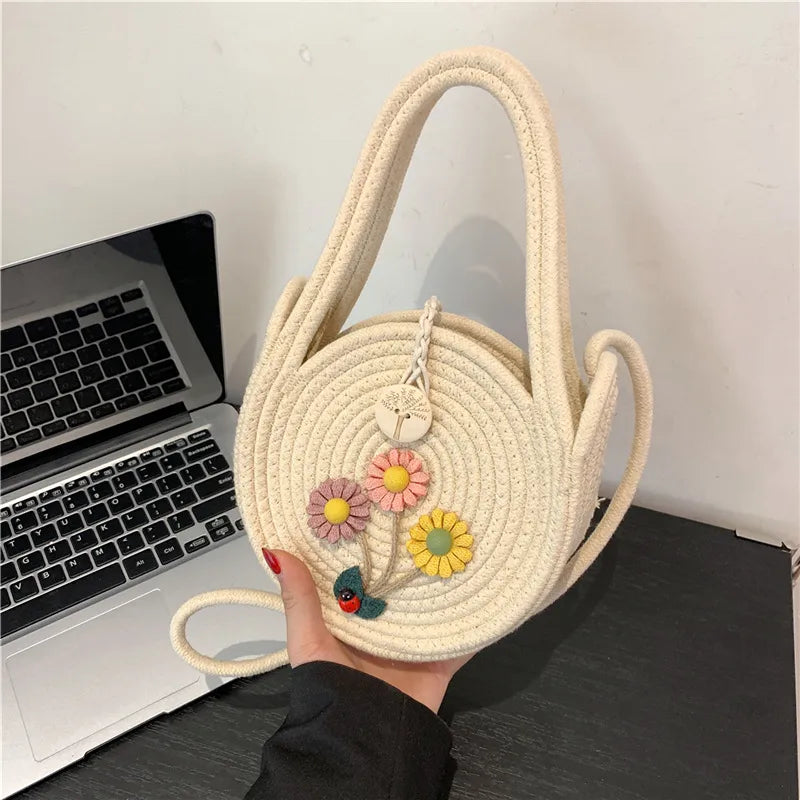 Round woven handbag with flower decoration – Cream flower bag held above a desk | BTendance