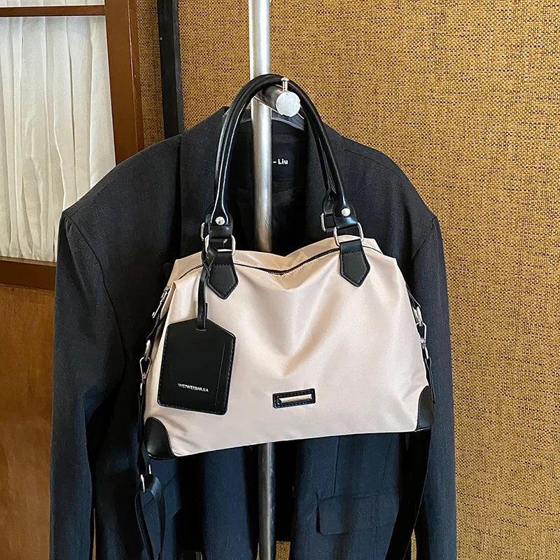 Nylon handbag with contrast handles and shoulder strap — cream with black trim on clothing display | BTendance