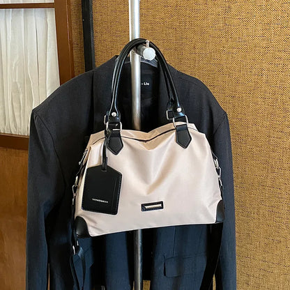 Nylon handbag with contrast handles and shoulder strap — cream with black trim on clothing display | BTendance