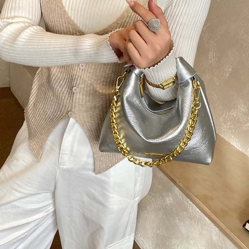 Soft handbag with gold tone chain – Silver bag held against a cream outfit | BTendance
