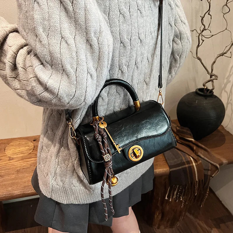 Structured top-handle flap handbag with round gold-tone clasp — black worn crossbody with scarf accent | BTendance