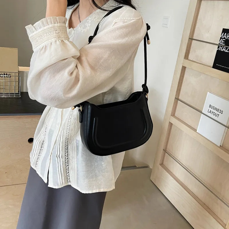 Curved shoulder bag with outlined front panel and knotted strap — black worn on shoulder | BTendance