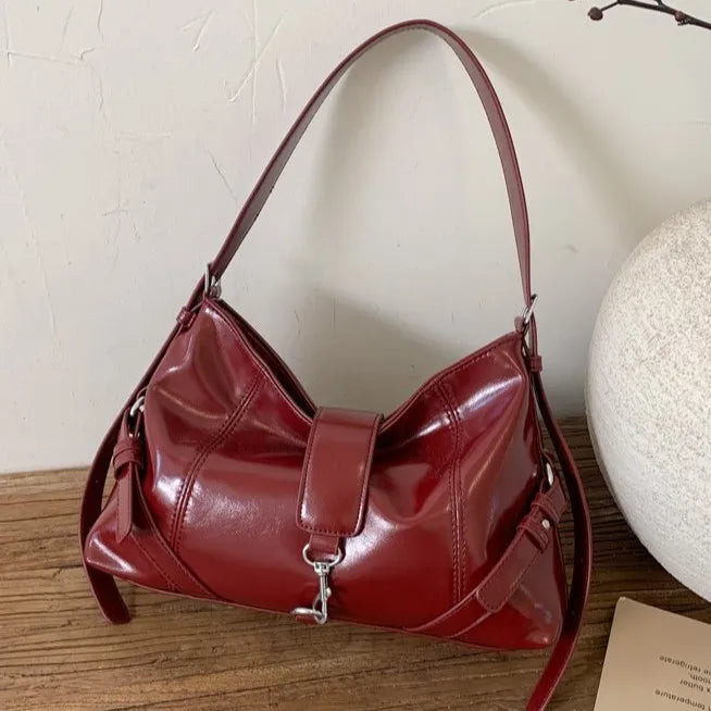 Glossy shoulder bag with central strap and metal clip — burgundy resting on cabinet | BTendance