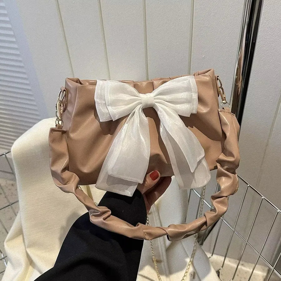 Bow-detail shoulder bag with gathered handle — tan with white bow held in one hand | BTendance