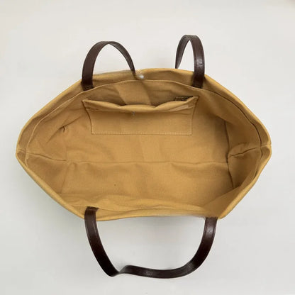 Wide canvas tote with contrasting dark shoulder handles — open tan interior showing small pocket | BTendance