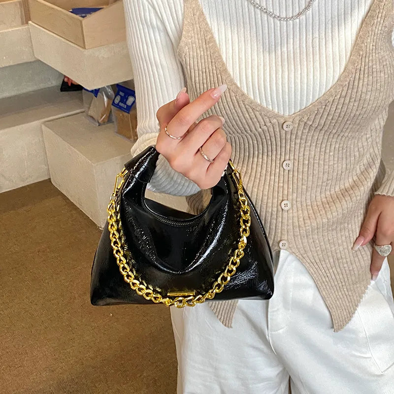 Soft handbag with gold tone chain – Black bag held against a knit top | BTendance