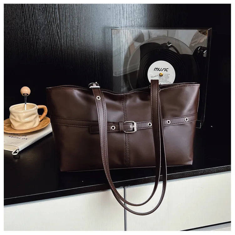 Rectangular shoulder tote with buckle and eyelet detailing — brown on cabinet beside cup | BTendance