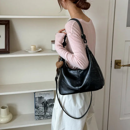 Slouchy shoulder bag with knotted strap and hanging charm — black worn on shoulder | BTendance