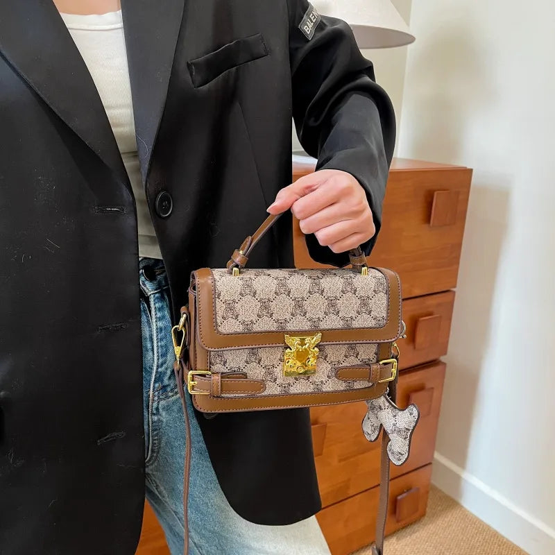 Bear pattern top handle bag with charm – Tan bag held with a black jacket | BTendance