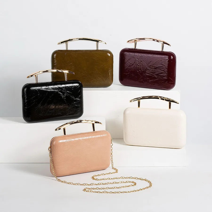 Textured rectangular evening bag with curved metal handle — five colors arranged on white display blocks | BTendance