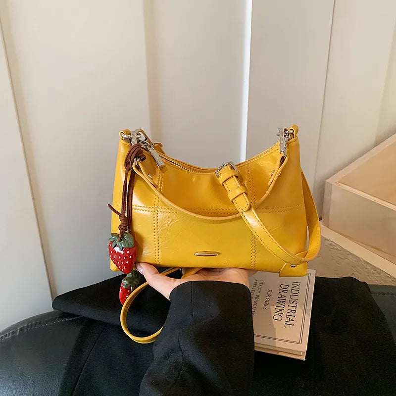 Glossy shoulder bag with strawberry charm – Yellow bag held in one hand | BTendance