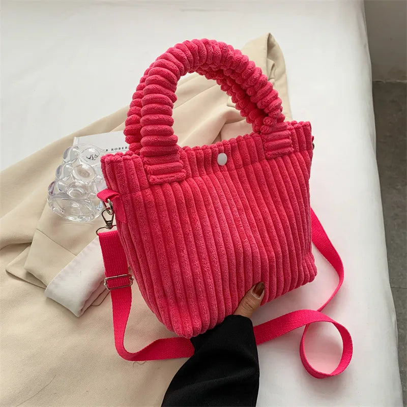 Ribbed plush handbag with rounded handles and long strap — bright pink held above fabric display | BTendance