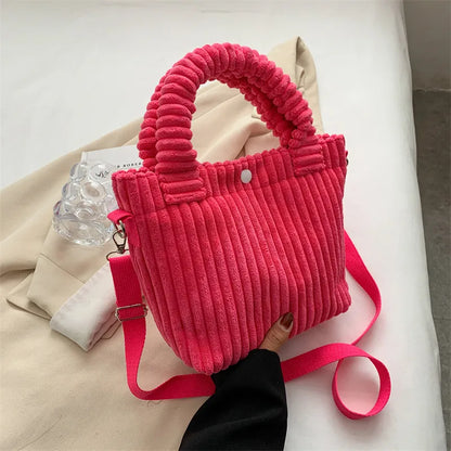 Ribbed plush handbag with rounded handles and long strap — bright pink held above fabric display | BTendance