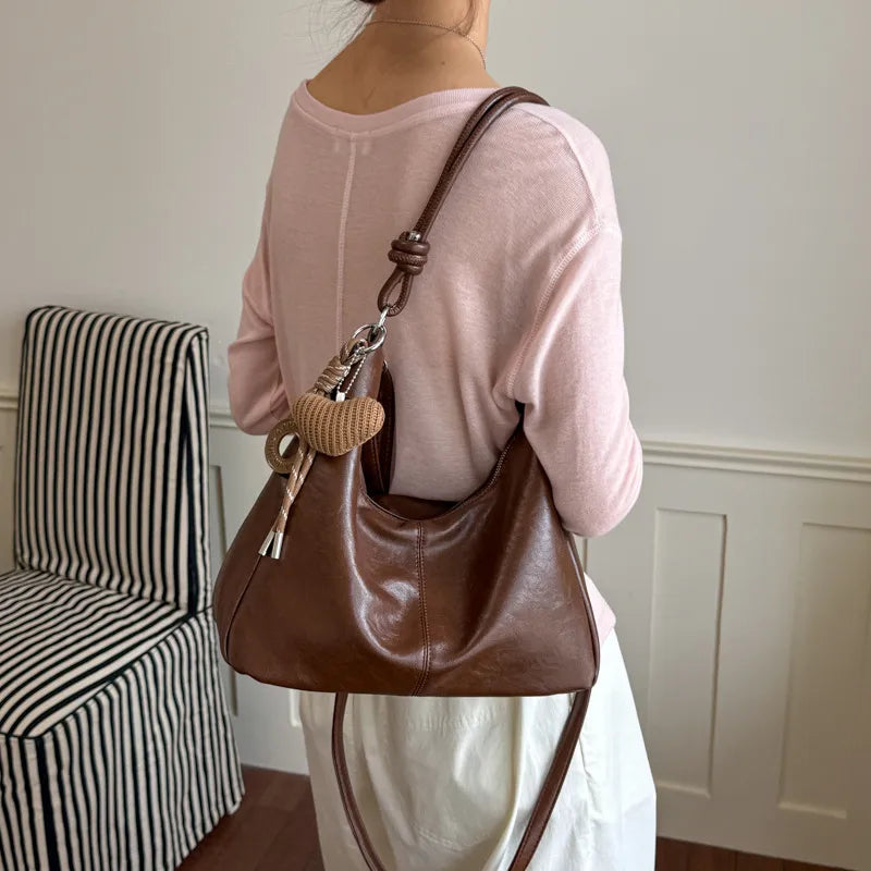 Slouchy shoulder bag with knotted strap and hanging charm — warm brown worn on shoulder | BTendance