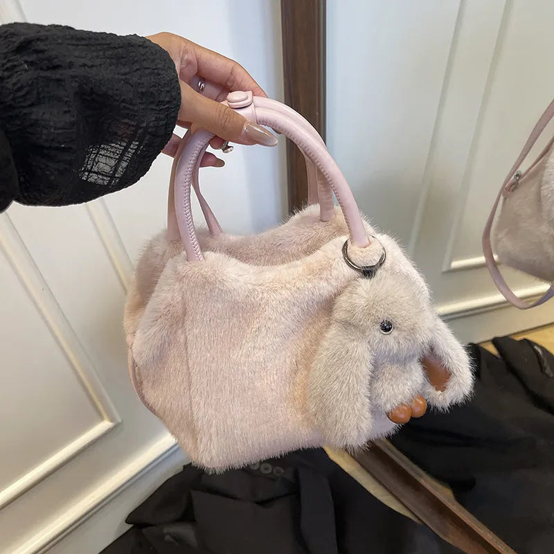 Plush top-handle handbag with rabbit charm — pale pink with pink handles held in one hand | BTendance