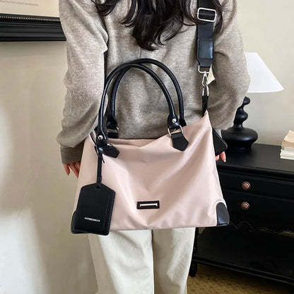 Nylon handbag with contrast handles and shoulder strap — pale pink with black trim worn crossbody | BTendance