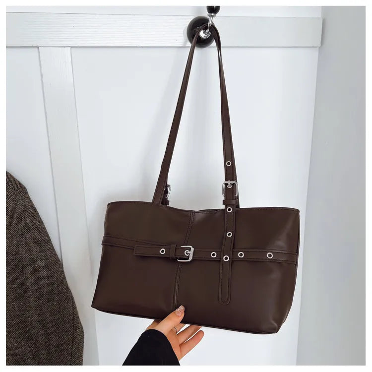 Rectangular shoulder tote with buckle and eyelet detailing — brown hanging against panelled wall | BTendance
