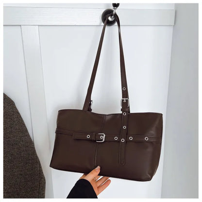 Rectangular shoulder tote with buckle and eyelet detailing — brown hanging against panelled wall | BTendance