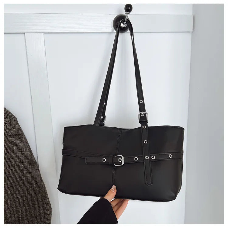 Rectangular shoulder tote with buckle and eyelet detailing — black hanging against panelled wall | BTendance