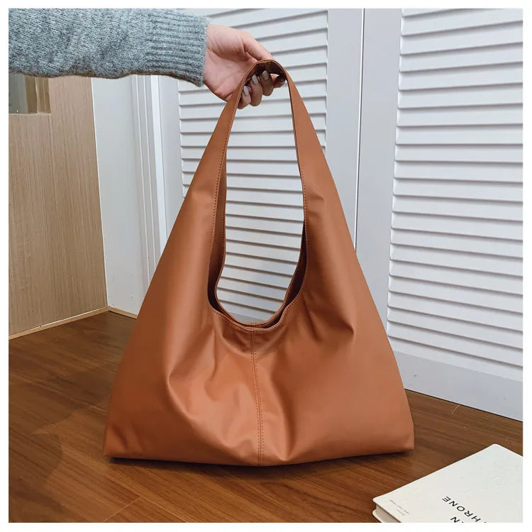 Slouchy shoulder tote with wide integrated strap — tan held above wooden table | BTendance