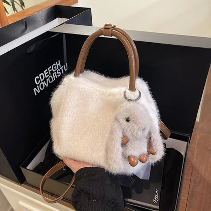 Plush top-handle handbag with rabbit charm — cream with tan handles held in one hand | BTendance